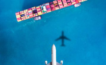 Airplane flying above cargo ship.